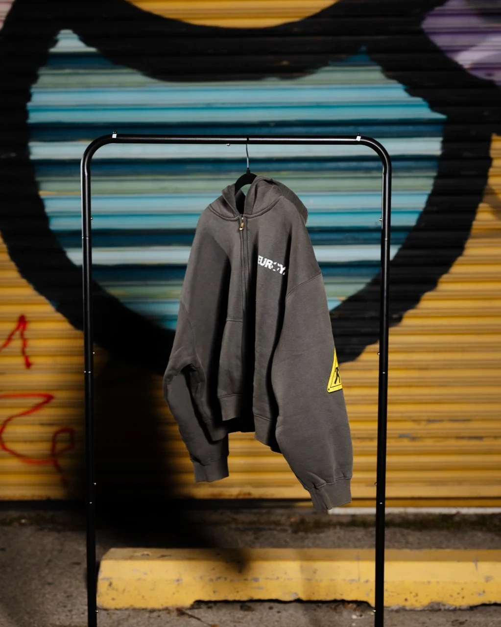 The washed-grey zip hoodie on the same rack against the painted shutter