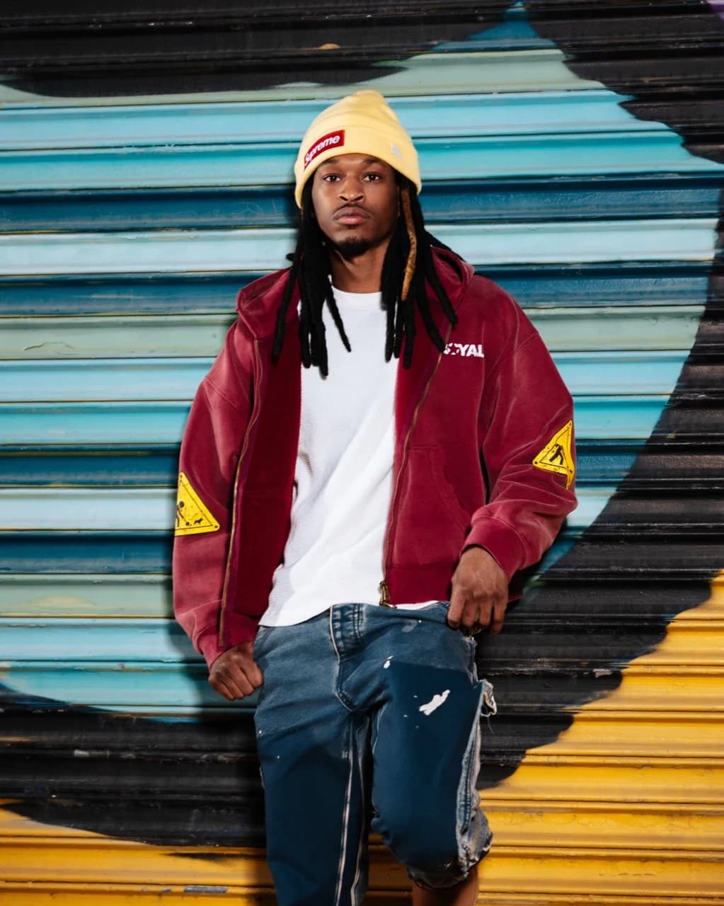 A model wearing the washed-red Bleu Royal zip hoodie in front of a painted roll-up shutter